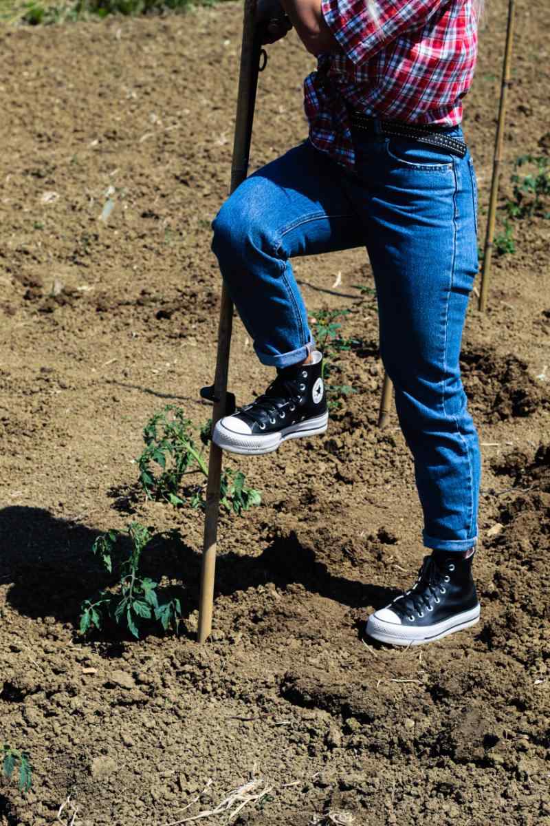 Persona che spinge con il piede sulla pedana del Piantacanne TechOrto per inserire il tutore nel terreno.